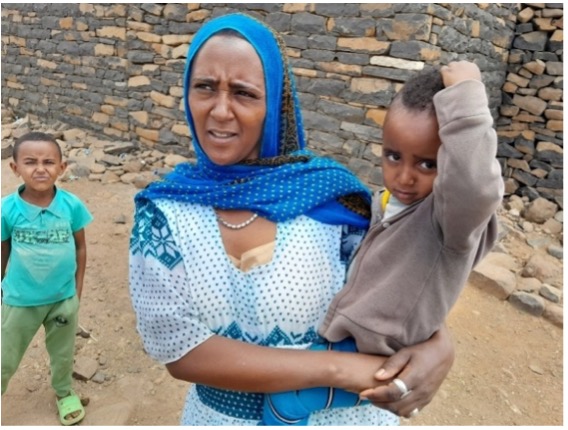 Mother Holding Child After Vaccination A mother holds her child close after receiving a vaccination, with another young sibling standing nearby. The family is pictured outside their home, illustrating the community's participation in vaccination efforts to protect children’s health.