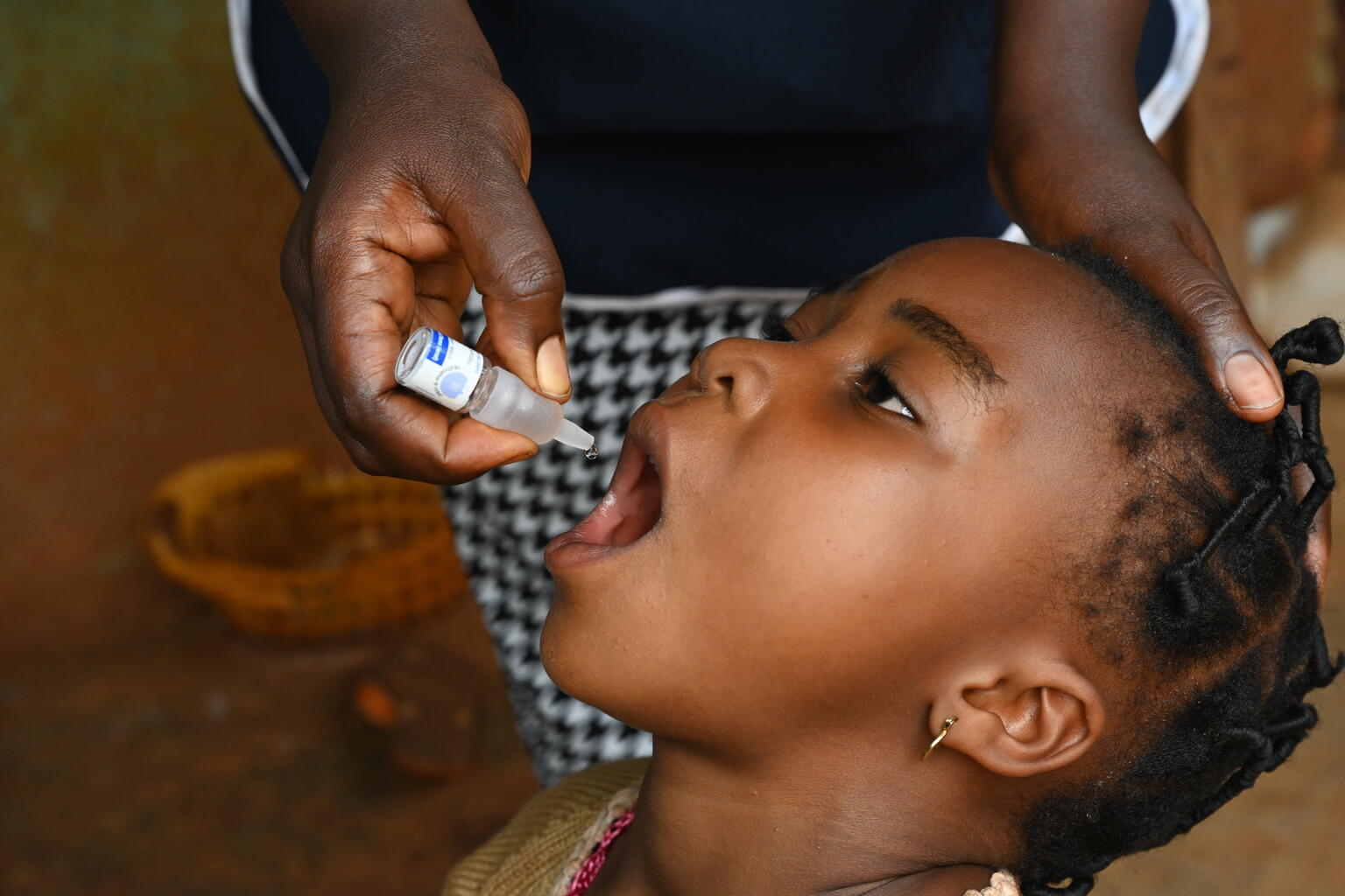 A young girl receiving oral polio vaccine administered by a health worker's hand.