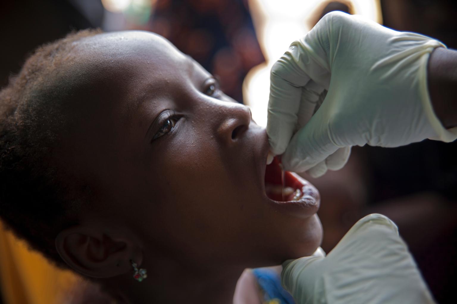 April 18, 2015, Madina Health Center, Guéckédou, Guinea. A girl swallows a vaccine against polio.