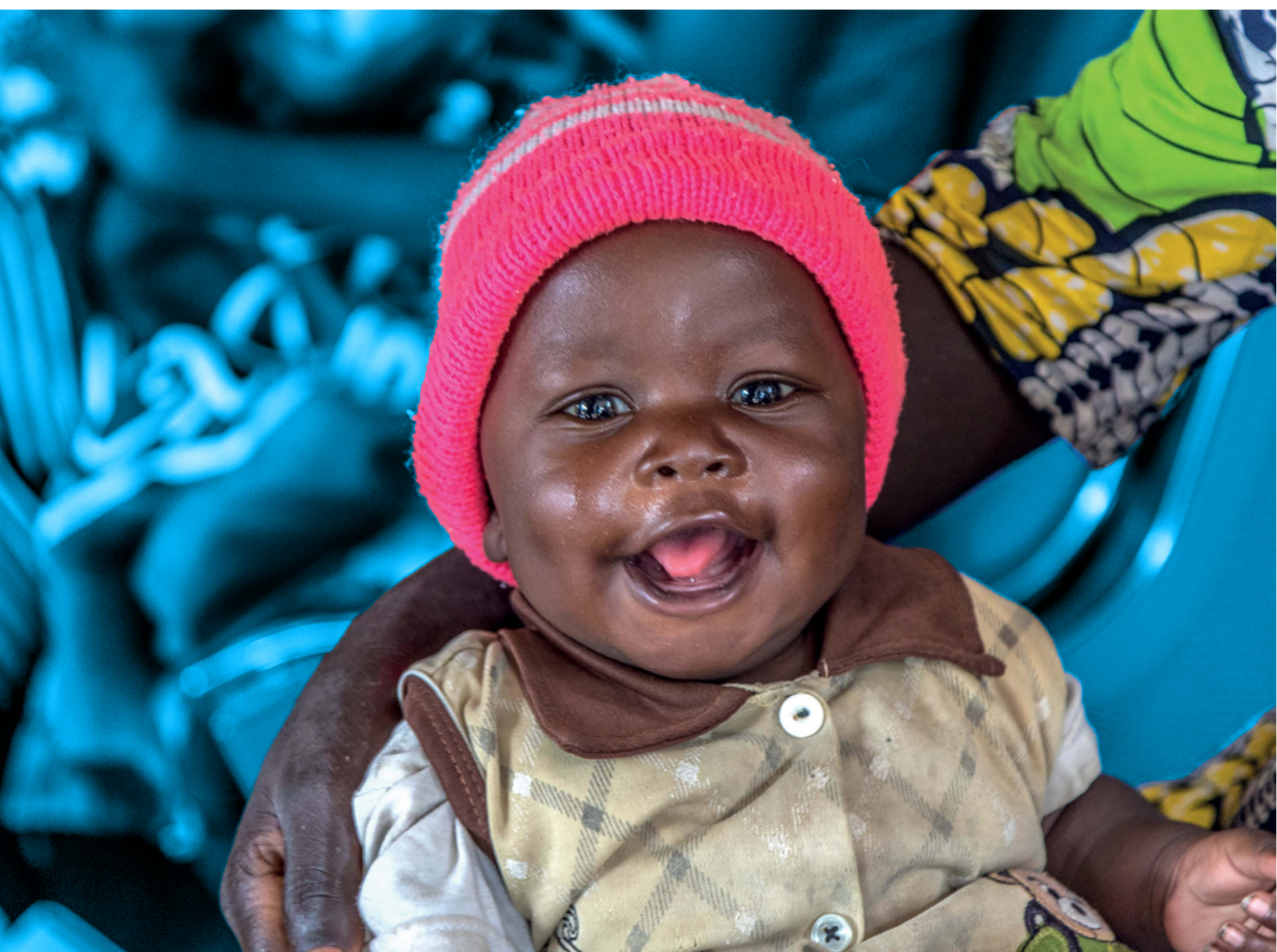 Smiling baby wearing a pink cap, held by a caregiver.