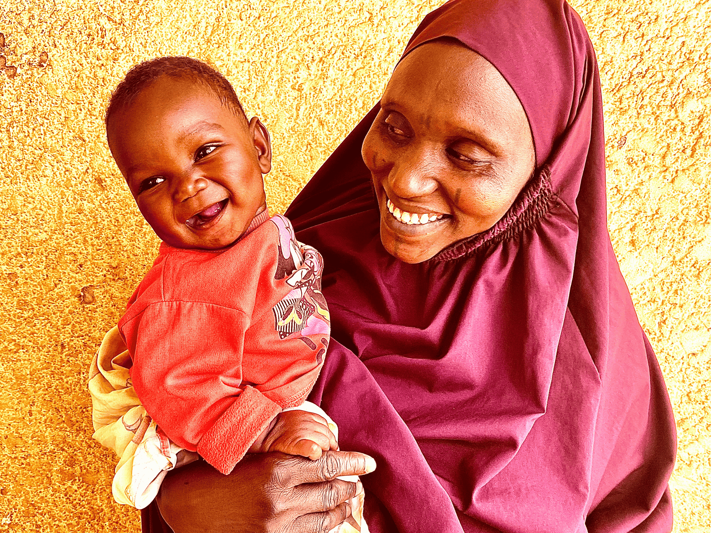 A smiling mother warmly holding her joyful baby, both radiating happiness against a vibrant yellow background.