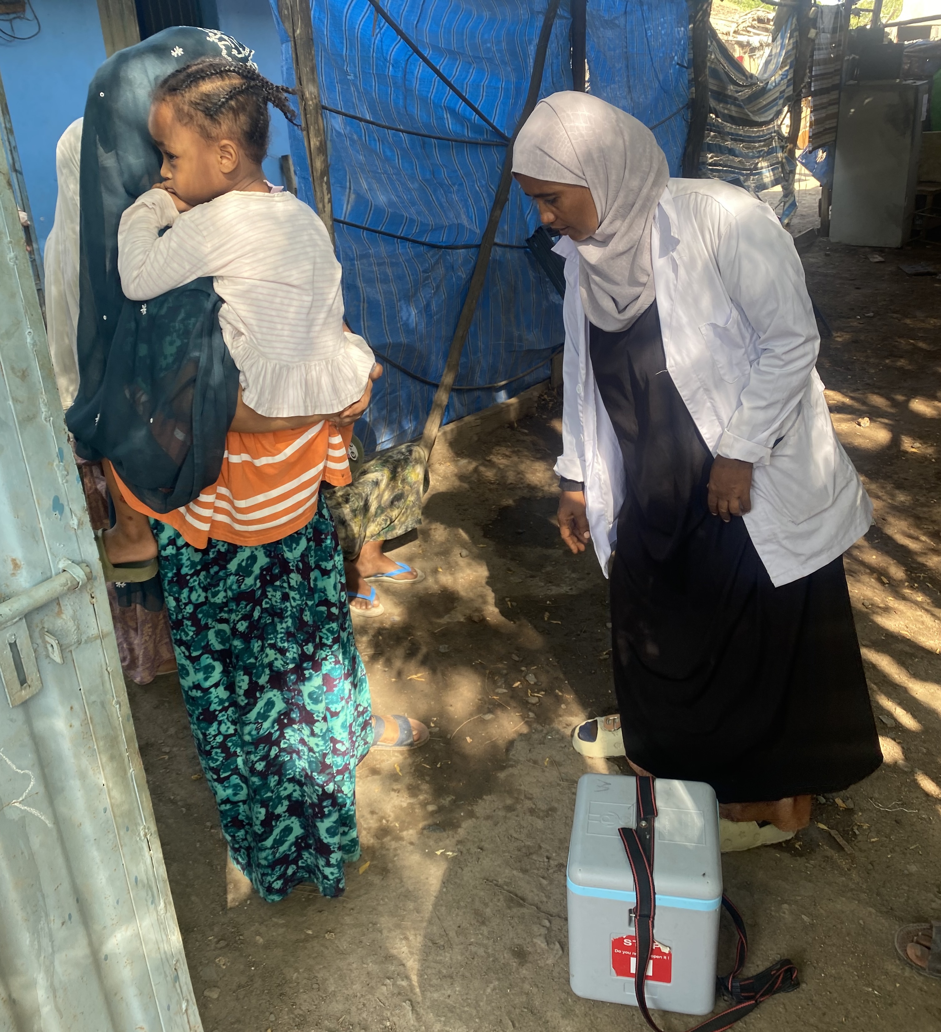 Ethiopia - door to door campaigns With a cold box of vaccines, Sister Mariyama Mohammed prepares to immunize a young child held by her mother. Her dedication ensures that Ethiopia’s health extension program reaches families directly, protecting children from preventable diseases.