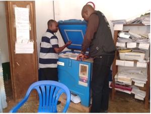Two healthcare workers inspect and prepare a cold chain storage unit to ensure the vaccines are kept at the correct temperature.