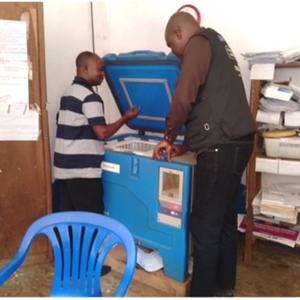 Two healthcare workers inspect and prepare a cold chain storage unit to ensure the vaccines are kept at the correct temperature.