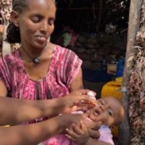 A mother smiles as her baby is vaccinated against polio in Ethiopia, showcasing local efforts to combat the disease.