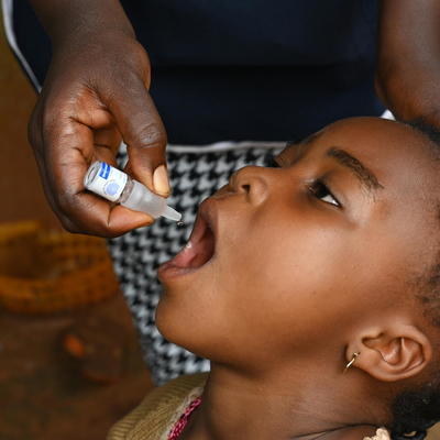 A young girl receiving oral polio vaccine administered by a health worker's hand.