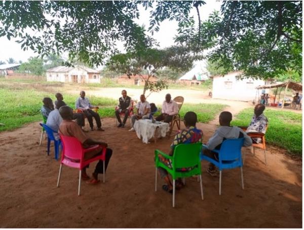A group of local leaders and community members hold a meeting under the shade of a tree to discuss ongoing polio eradication efforts in their village.