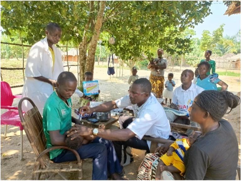 A healthcare professional administers polio drops to a child, while a community health worker assists during an outreach session in the village.