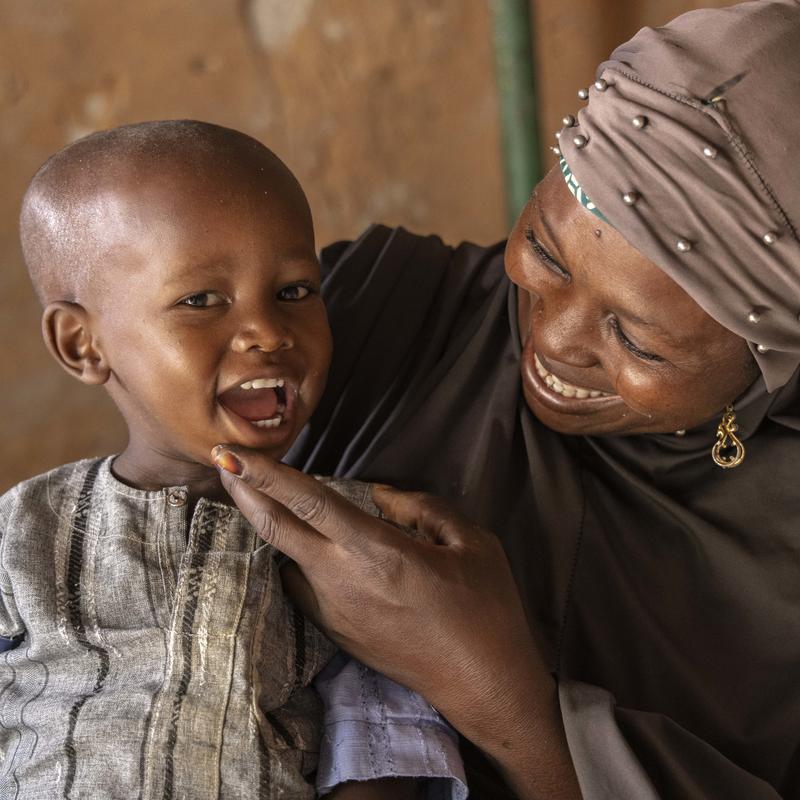 Une femme nigérienne tient un enfant souriant. La femme porte un foulard et l'enfant a la main sur le menton.
