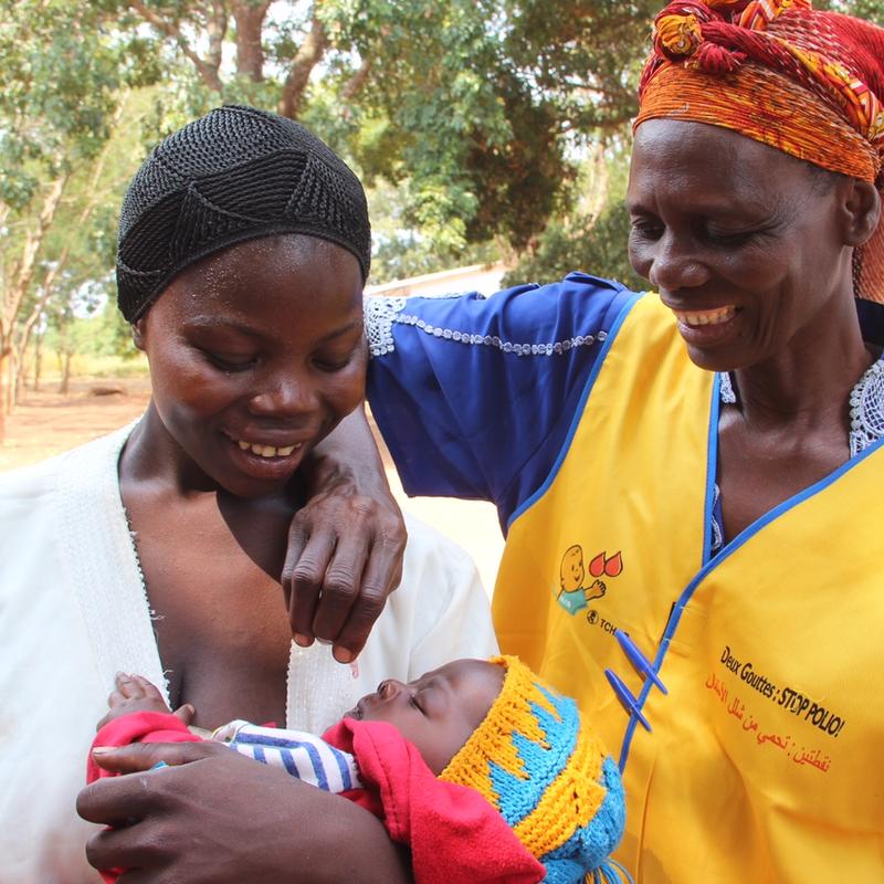 Two women smiling—one holding a baby, the other administering a vaccine