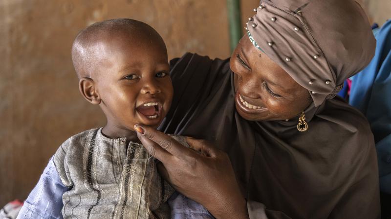 Une femme nigérienne tient un enfant souriant. La femme porte un foulard et l'enfant a la main sur le menton.